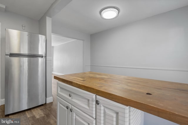 kitchen featuring dark wood-type flooring, wooden counters, stainless steel fridge, and white cabinetry