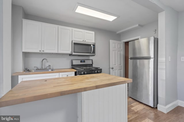 kitchen with butcher block countertops, light hardwood / wood-style floors, stainless steel appliances, sink, and white cabinets