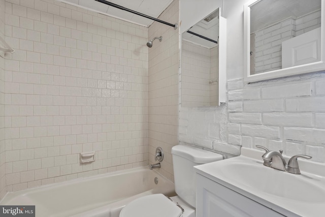 full bathroom featuring tiled shower / bath, vanity, toilet, and tile walls