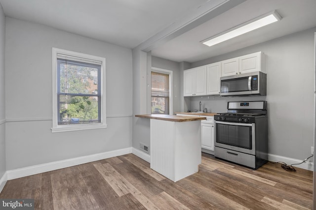 kitchen with appliances with stainless steel finishes, wood-type flooring, kitchen peninsula, and white cabinets