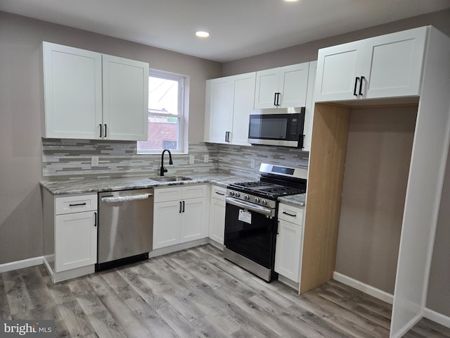 kitchen with white cabinetry, sink, light stone countertops, appliances with stainless steel finishes, and light hardwood / wood-style floors