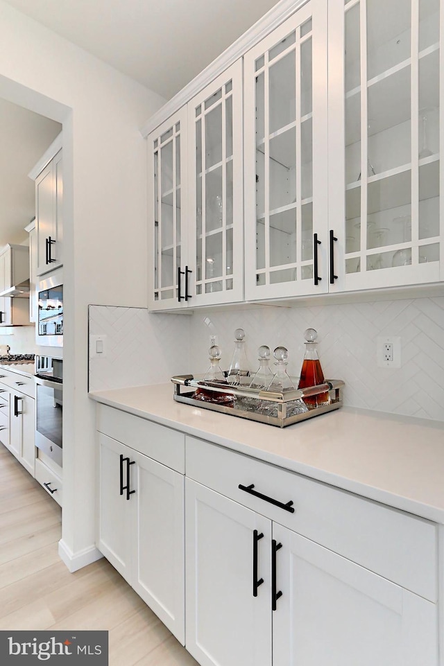 bar featuring decorative backsplash, stainless steel appliances, white cabinetry, and light wood-type flooring