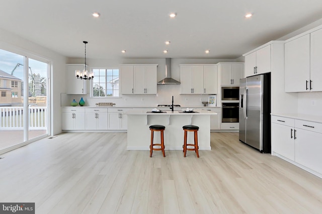 kitchen with wall chimney exhaust hood, white cabinetry, stainless steel appliances, and plenty of natural light