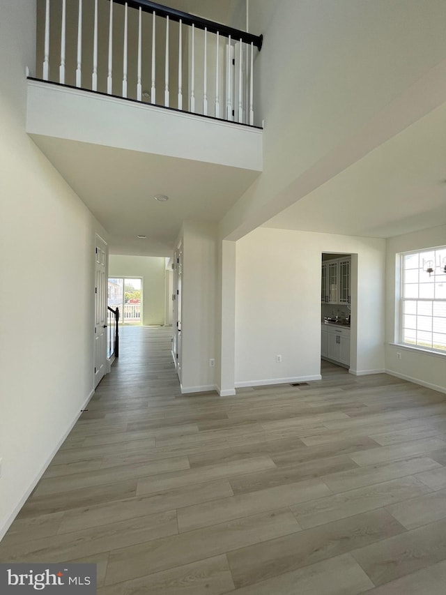 interior space with light hardwood / wood-style flooring, a towering ceiling, a chandelier, and a healthy amount of sunlight