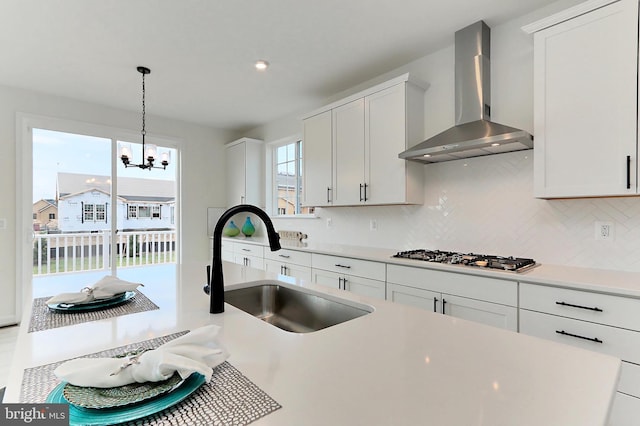 kitchen featuring white cabinets, stainless steel gas cooktop, an inviting chandelier, sink, and wall chimney range hood