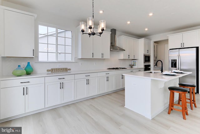 kitchen with an inviting chandelier, sink, wall chimney range hood, and white cabinetry