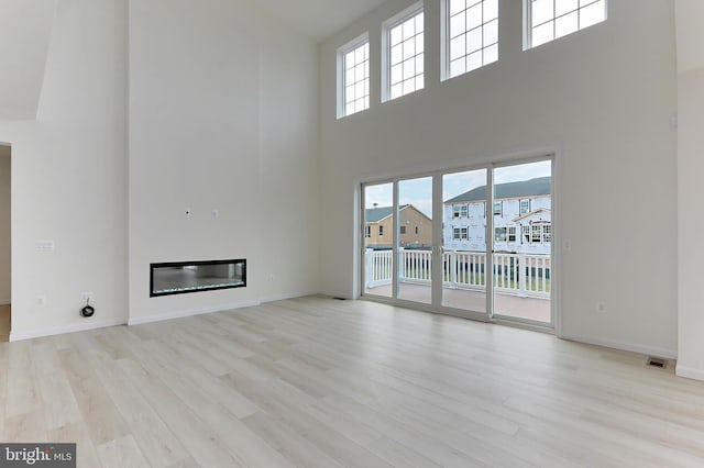 unfurnished living room with a high ceiling, light hardwood / wood-style floors, and a healthy amount of sunlight