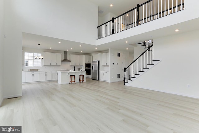 unfurnished living room with an inviting chandelier, light hardwood / wood-style floors, and a towering ceiling