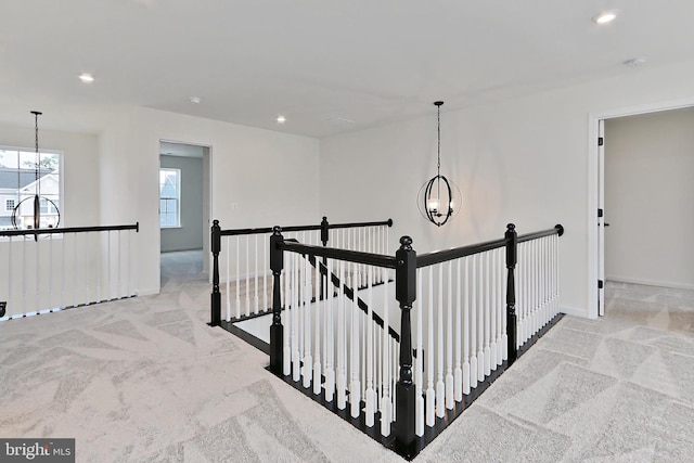 hallway with an inviting chandelier and light colored carpet