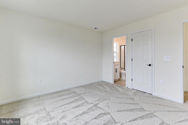 unfurnished bedroom featuring light carpet and ensuite bathroom