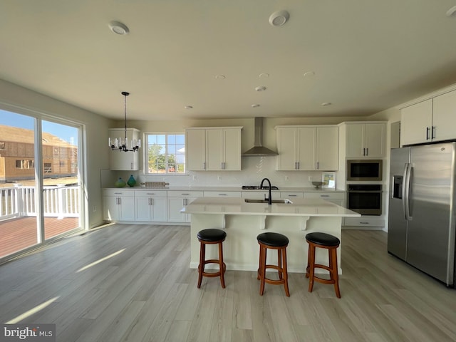 kitchen featuring light wood-type flooring, white cabinetry, hanging light fixtures, wall chimney range hood, and appliances with stainless steel finishes