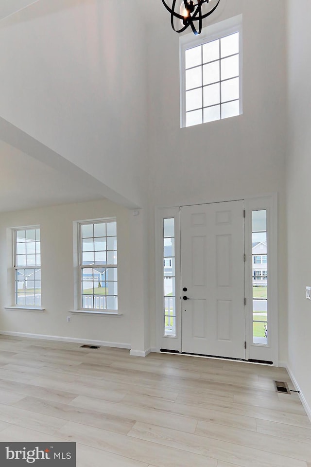 foyer featuring a towering ceiling, light wood-type flooring, and plenty of natural light