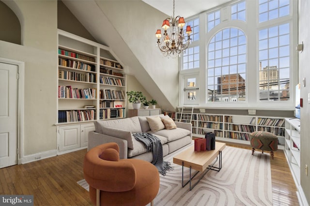 sitting room with hardwood / wood-style flooring, baseboards, built in features, a high ceiling, and an inviting chandelier