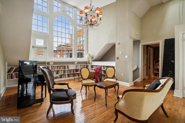 living area with baseboards, a notable chandelier, a towering ceiling, and hardwood / wood-style floors