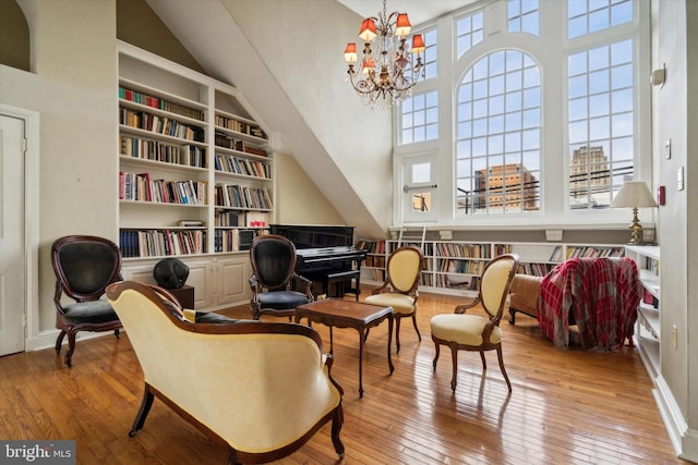 living area with hardwood / wood-style floors, high vaulted ceiling, an inviting chandelier, and built in shelves