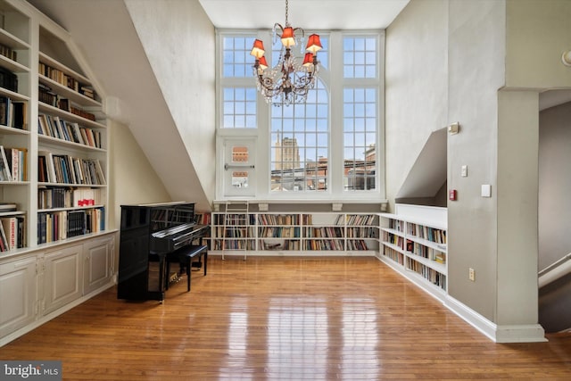 living area featuring built in features, baseboards, an inviting chandelier, and wood-type flooring