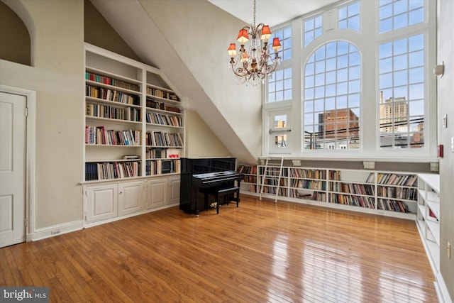 living area with wood-type flooring, high vaulted ceiling, baseboards, a chandelier, and built in shelves
