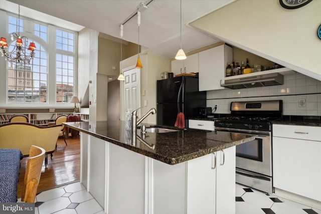 kitchen featuring decorative backsplash, under cabinet range hood, stainless steel gas range oven, a sink, and freestanding refrigerator