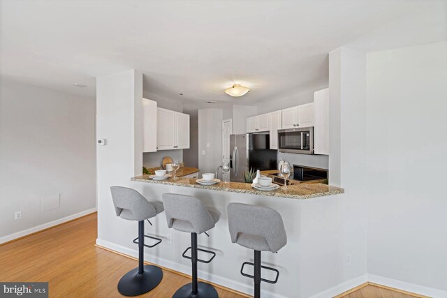 kitchen featuring a breakfast bar, kitchen peninsula, stainless steel appliances, light wood-type flooring, and white cabinets