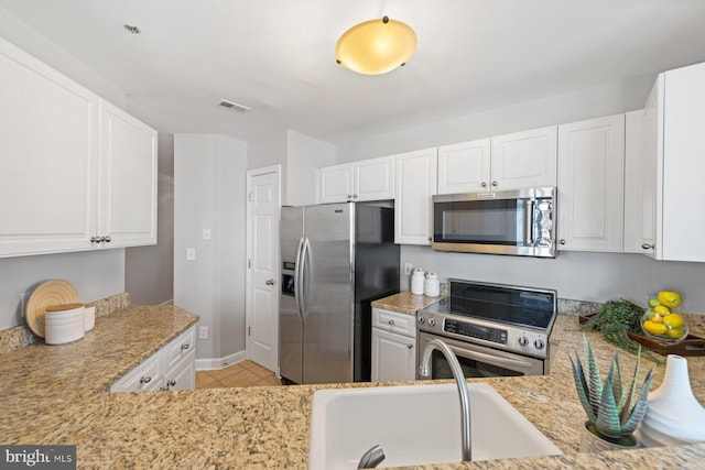 kitchen with stainless steel appliances, light tile patterned floors, white cabinets, and light stone countertops