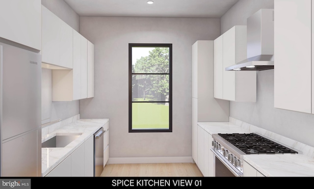 kitchen featuring wall chimney range hood, stainless steel appliances, sink, light stone countertops, and white cabinets