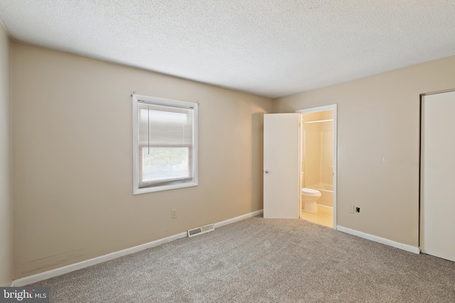 unfurnished bedroom featuring a textured ceiling, ensuite bath, and carpet