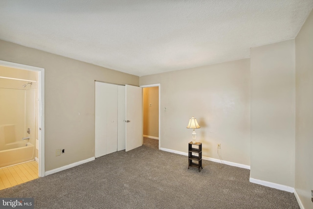 unfurnished bedroom with a textured ceiling, connected bathroom, dark colored carpet, and a closet