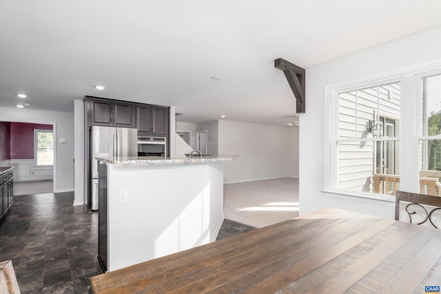 kitchen featuring stainless steel appliances, light stone countertops, and dark brown cabinets