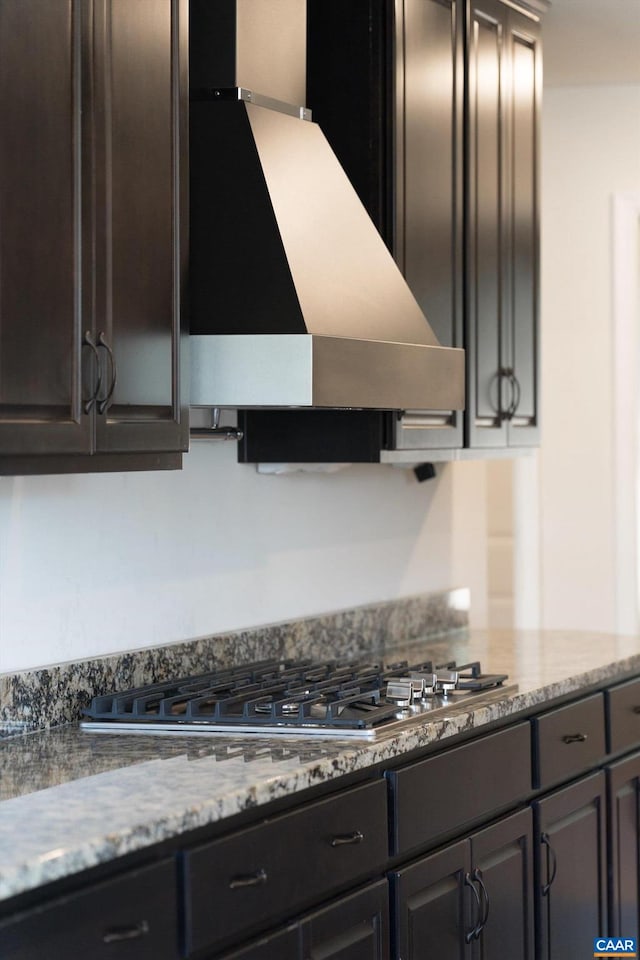 kitchen with stainless steel gas stovetop, light stone counters, exhaust hood, and dark brown cabinets