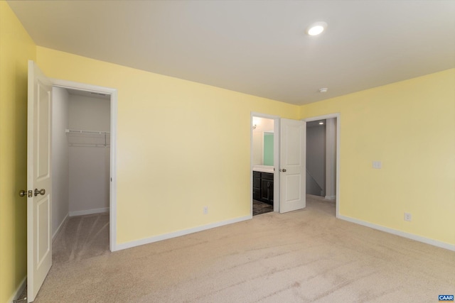 unfurnished bedroom featuring a walk in closet, ensuite bathroom, light colored carpet, and a closet