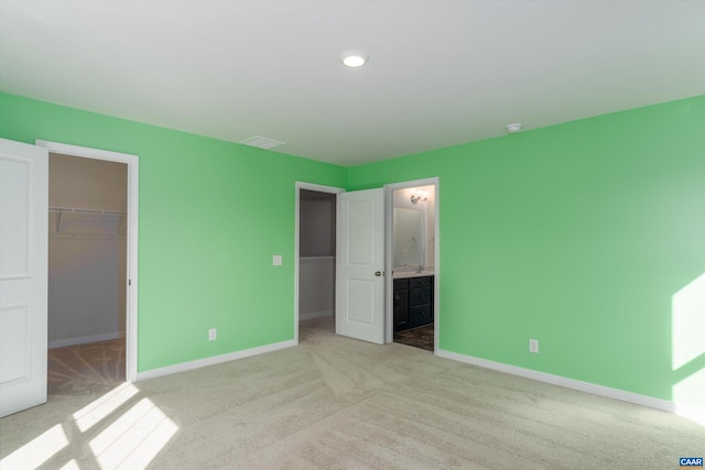 unfurnished bedroom with light colored carpet, connected bathroom, a spacious closet, and a closet