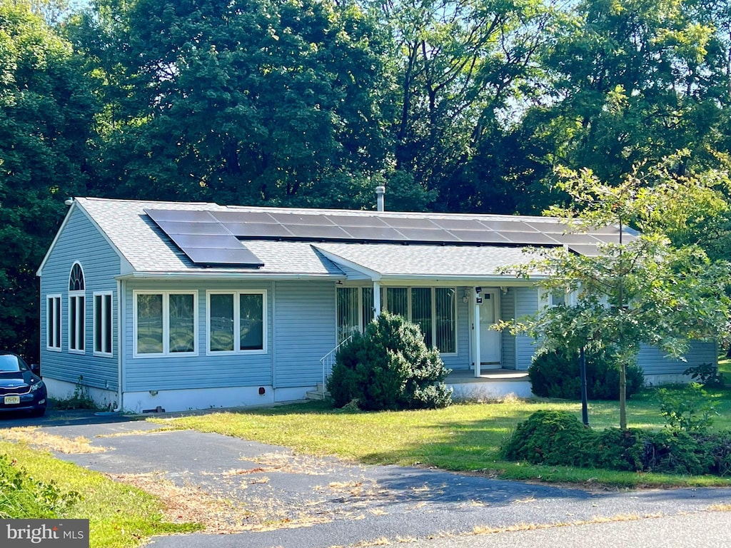 single story home with a front yard, solar panels, and covered porch