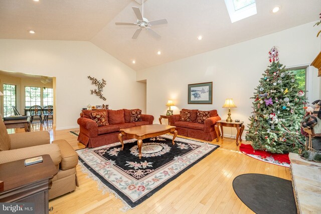 living room featuring wood-type flooring, a skylight, high vaulted ceiling, and ceiling fan