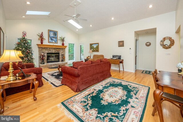 living room with ceiling fan, a skylight, a stone fireplace, high vaulted ceiling, and hardwood / wood-style flooring