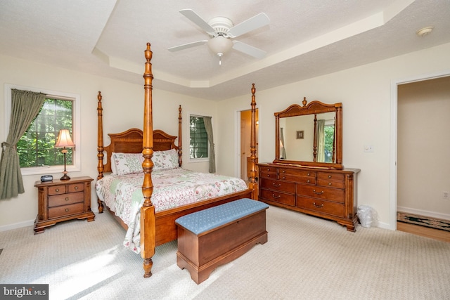 bedroom with ceiling fan, a textured ceiling, a raised ceiling, and light carpet