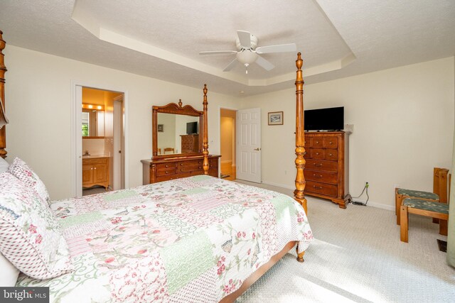 carpeted bedroom with ensuite bath, ceiling fan, a tray ceiling, and a textured ceiling