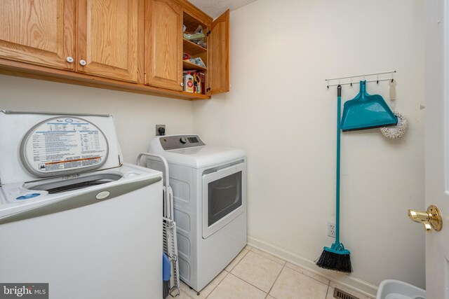 laundry room with washer and clothes dryer, light tile patterned floors, and cabinets