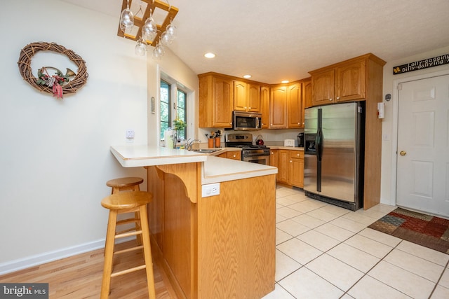 kitchen with sink, kitchen peninsula, a kitchen breakfast bar, stainless steel appliances, and light tile patterned floors