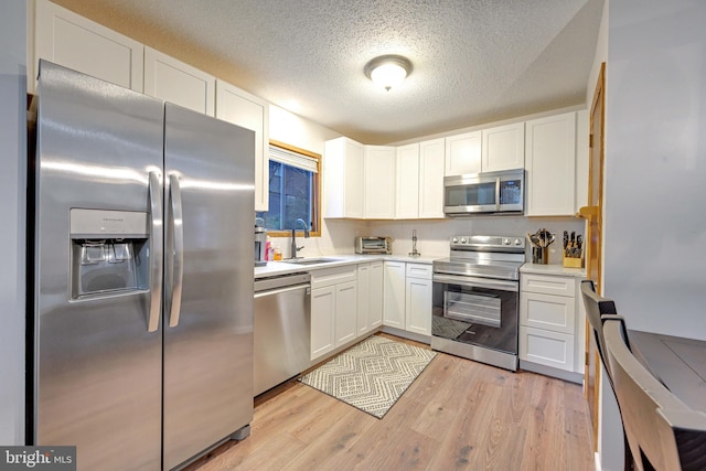 kitchen featuring white cabinets, stainless steel appliances, light wood-type flooring, and sink