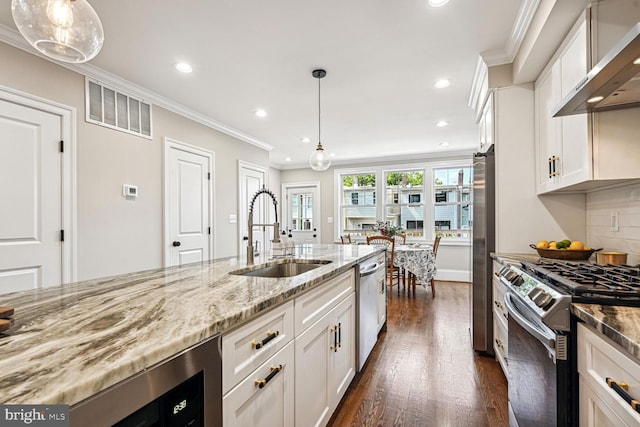 kitchen with appliances with stainless steel finishes, white cabinets, wall chimney exhaust hood, decorative light fixtures, and sink