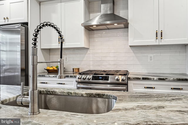 kitchen featuring light stone counters, stainless steel appliances, wall chimney range hood, and white cabinetry