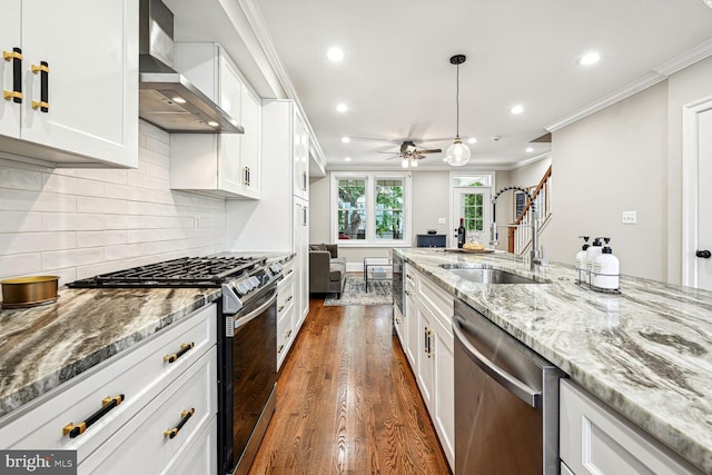 kitchen featuring appliances with stainless steel finishes, dark wood-type flooring, white cabinets, sink, and wall chimney range hood