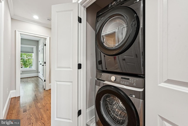 laundry room featuring wood-type flooring, stacked washer and clothes dryer, and ornamental molding