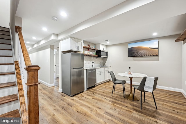 kitchen with appliances with stainless steel finishes, light wood-type flooring, white cabinetry, and decorative backsplash