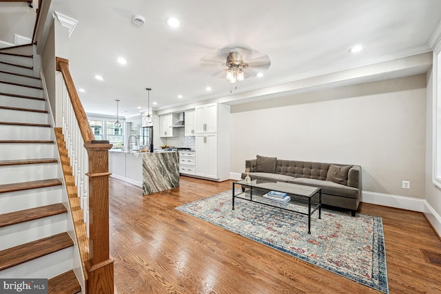 living room with ceiling fan, light wood-type flooring, crown molding, and sink