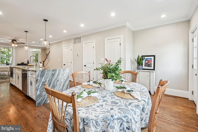 dining space with ceiling fan, sink, crown molding, and dark wood-type flooring