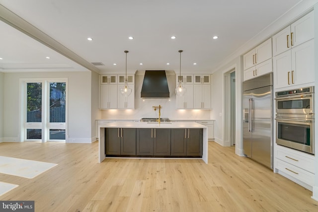 kitchen with white cabinets, custom exhaust hood, decorative light fixtures, and appliances with stainless steel finishes