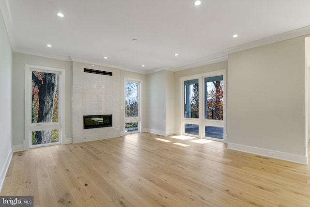 unfurnished living room featuring a tile fireplace, light hardwood / wood-style flooring, a healthy amount of sunlight, and ornamental molding