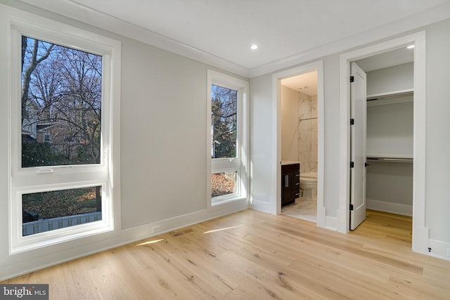 unfurnished bedroom featuring a closet, light hardwood / wood-style floors, ensuite bath, and a spacious closet