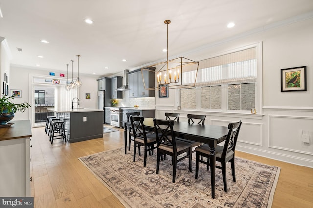 dining area with ornamental molding, sink, light hardwood / wood-style flooring, and a chandelier